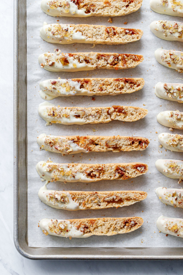 Overhead of white chocolate-dipped biscotti cookies lined up on a baking sheet