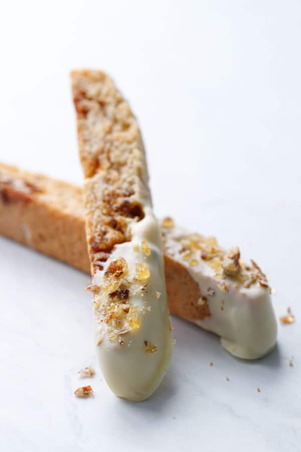 Two white chocolate-dipped biscotti cookies, crossed on top of each other on a marble background
