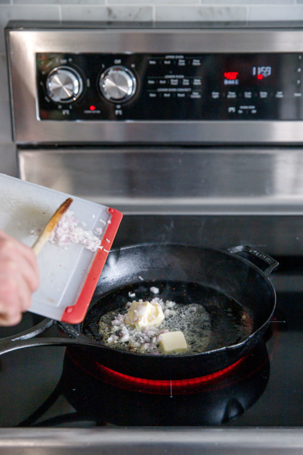 Adding shallot and butter to a hot cast iron skillet on a stove