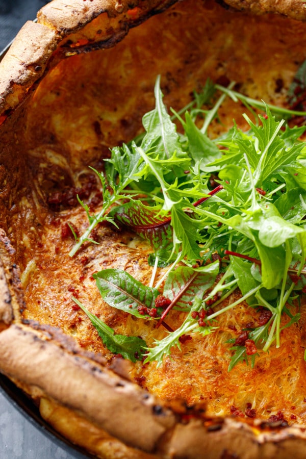 Closeup of a skillet Dutch baby with melted cheeze, chorizo and a pile of baby lettuce in the middle
