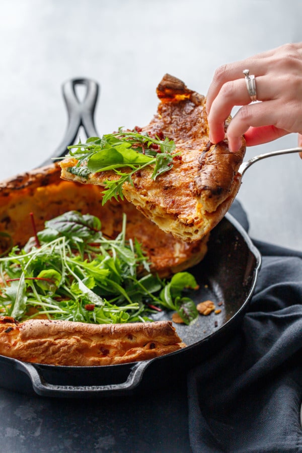 Hand lifting out a slice of a savory Dutch baby, showing the layers.