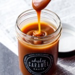 A spoon drizzling homemade whiskey caramel sauce into a jar full of caramel