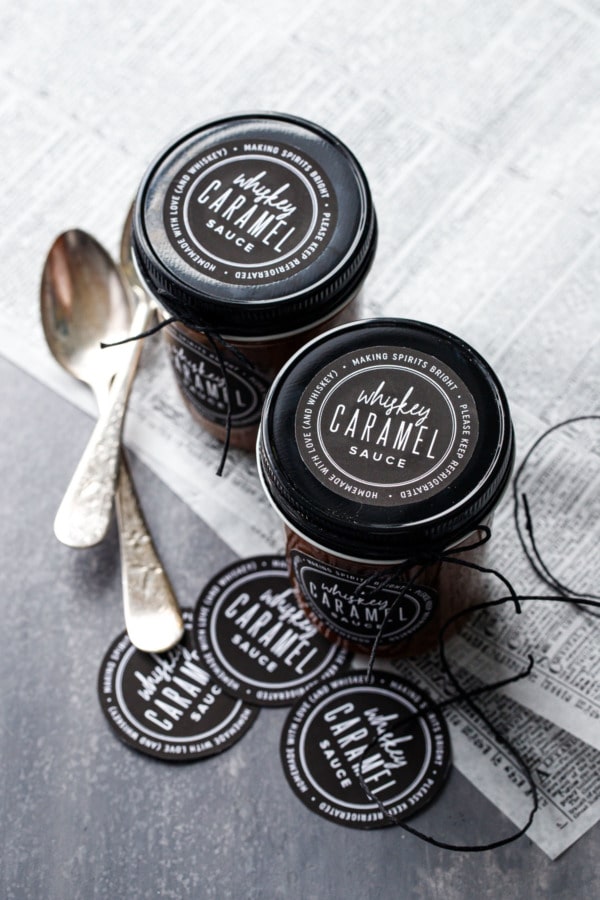 Zwei Gläser voll mit selbstgemachter Whiskey-Karamellsauce, mit schwarzen Deckeln und bedruckbaren schwarz-weißen Etiketten, gebunden mit schwarzer Schnur.