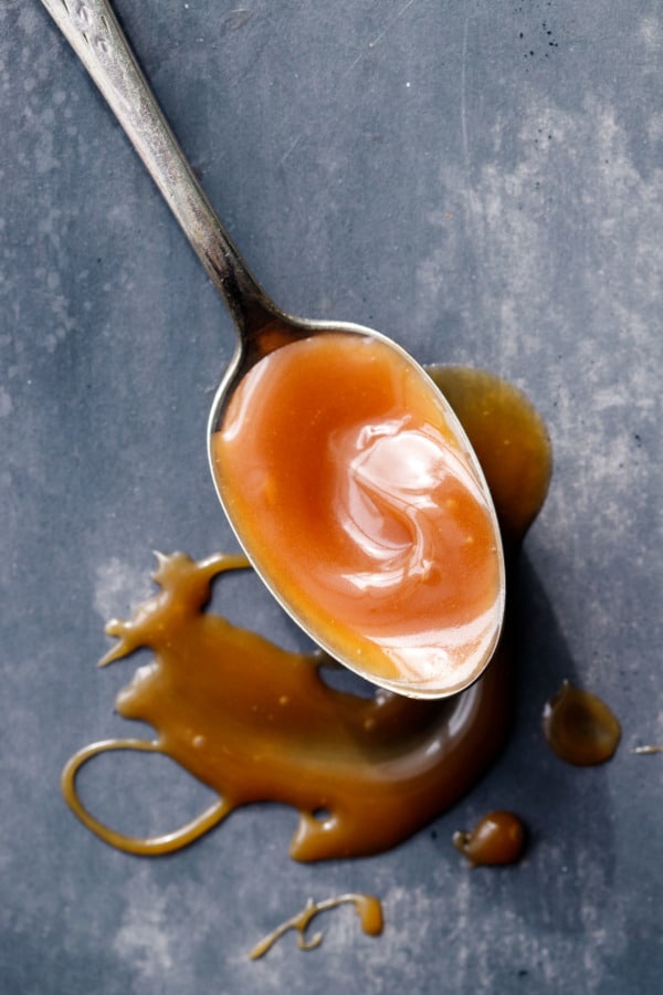 Une cuillère pleine de sauce caramel au whisky, arrosée de façon désordonnée sur un fond peint en gris.