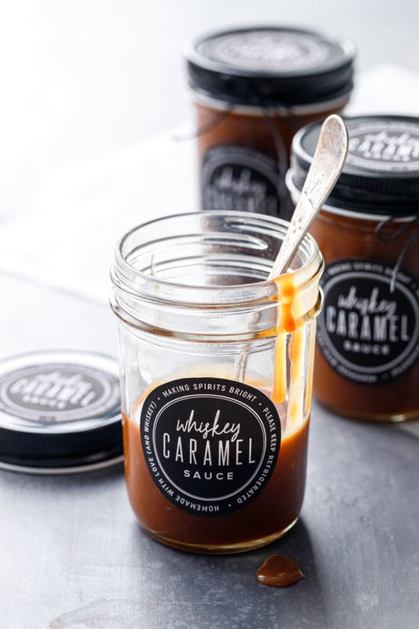 Three jars of homemade whiskey caramel sauce, one jar mostly empty with a few drips, and printed black and white labels.