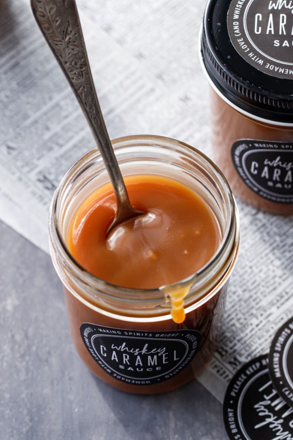 Looking down at a jar full of whiskey caramel sauce with a spoon inside.