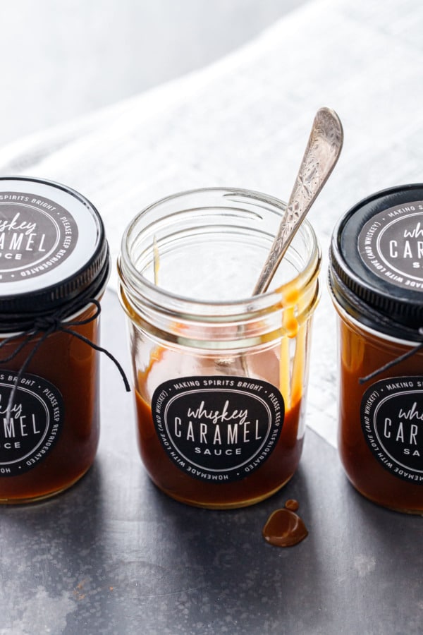 Three backlit jars of whiskey caramel sauce, with a spoon in one partially-empty jar and drips of caramel on the rim.