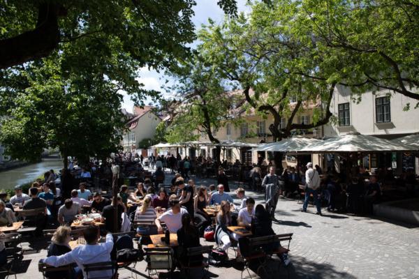 Busy promenade in Ljubljana, Slovenia, filled with people eating at cafes on a sunny day.