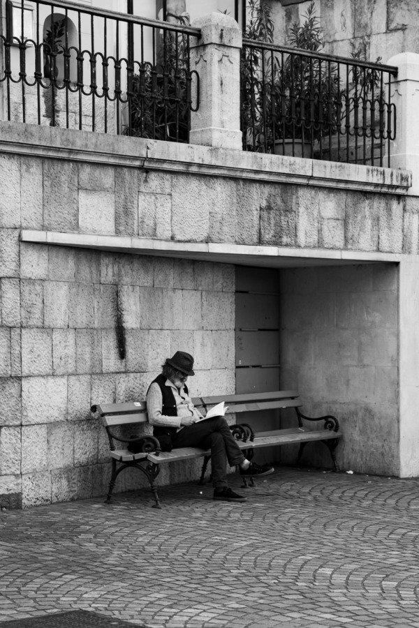 Black and white photo of an old man reading on a bench in Ljubljana, Slovenia