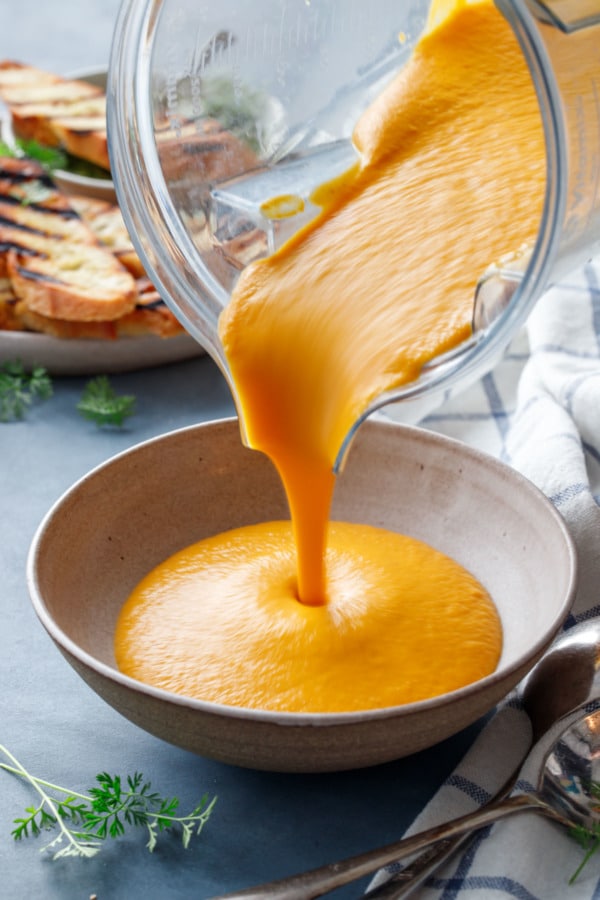 Pouring creamy carrot soup from a blender into a ceramic bowl.