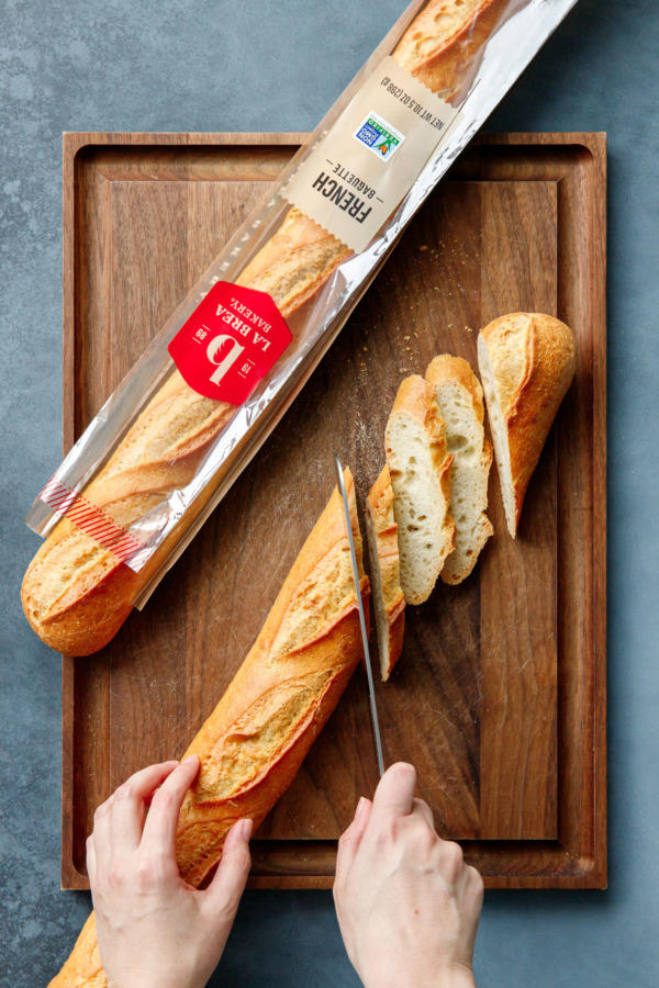 Cutitng a baguette diagonally on a wooden cutting board.