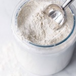 Flour in a glass container with a metal scoop.