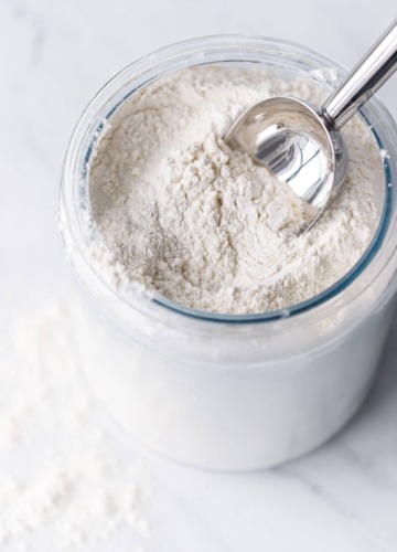 Flour in a glass container with a metal scoop.