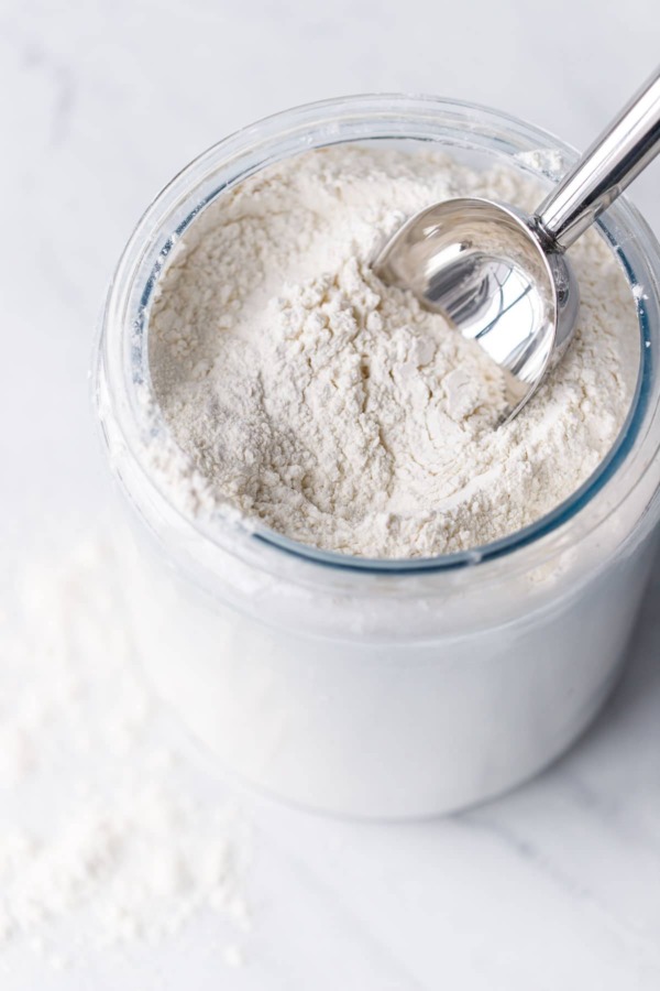 Flour in a glass container with a metal scoop.