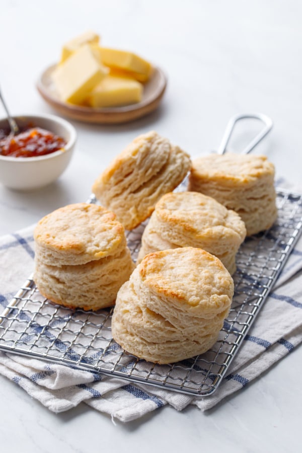 Tall, flaky sourdough biscuits on a cooling rack with butter and marmalade