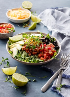 Turkey Taco Bowls with Cilantro Rice on a dark blue background with bowls of salsa and cheese and slices of lime scattered around.