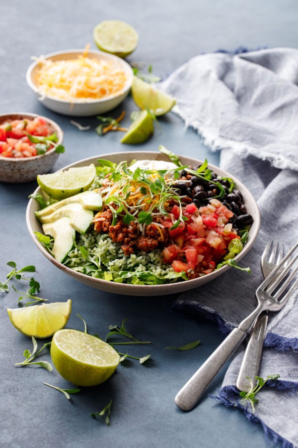 Turkey Taco Bowls with Cilantro Rice on a dark blue background with bowls of salsa and cheese and slices of lime scattered around.