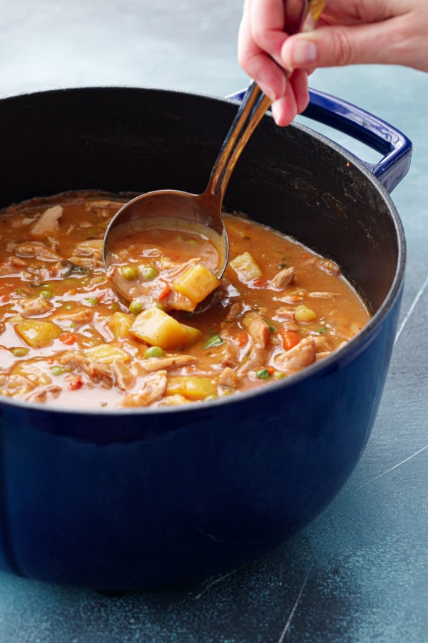 Dutch oven with turkey stew, lifting a ladleful of stew.