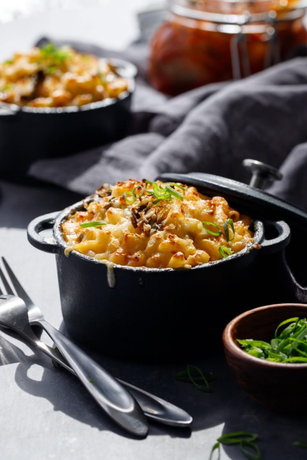 Creamy white cheddar Macaroni & Cheese with Kimchi in black ramekins with sliced scallion