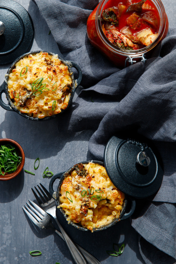 Overhead shot of Mac'n Kimcheese in black ramekins with a jar of kimchi and scallions