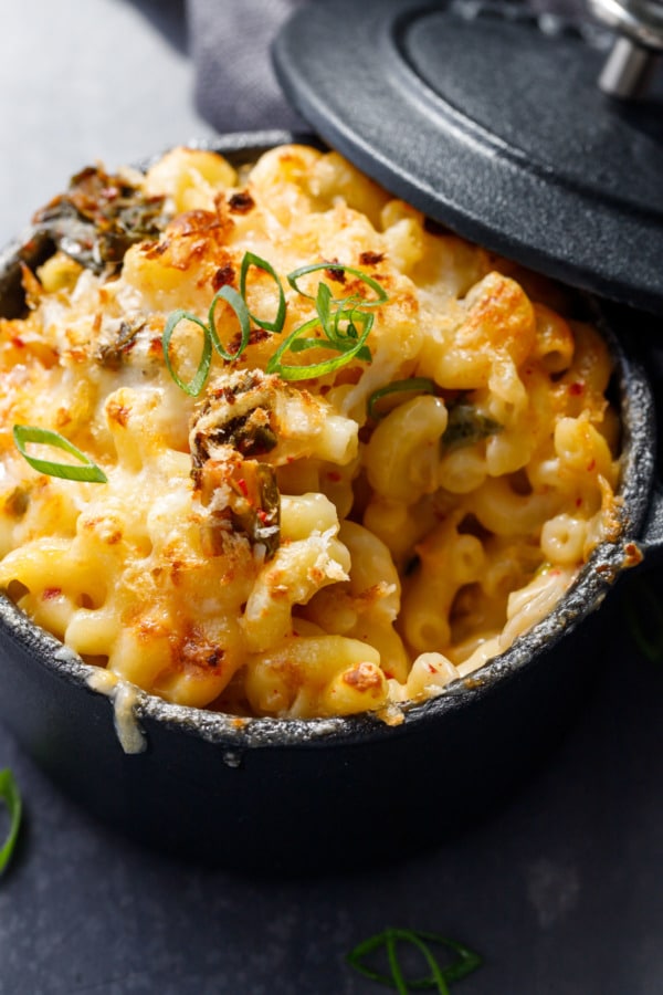 Closeup cocotte of Kimchee Macaroni & Cheese in black ramekins with a jar of kimchi