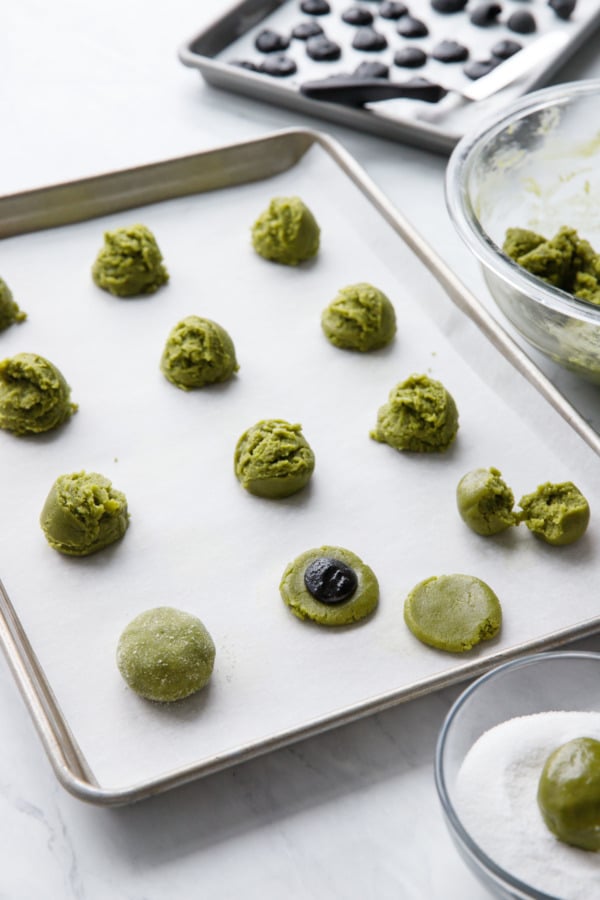 Balls of matcha cookie dough on a cookie sheet, being stuffed with black sesame paste