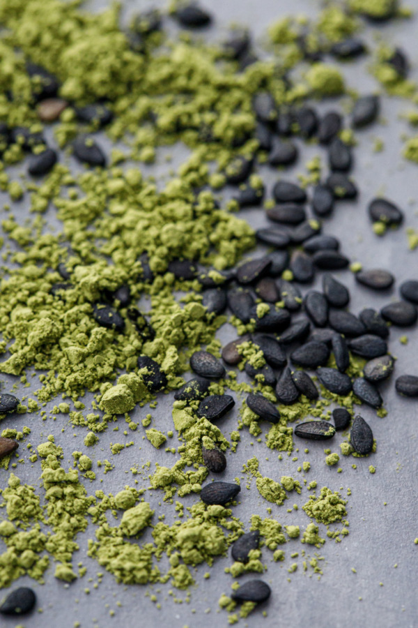 Extreme closeup of matcha powder and black sesame seeds on a gray background.