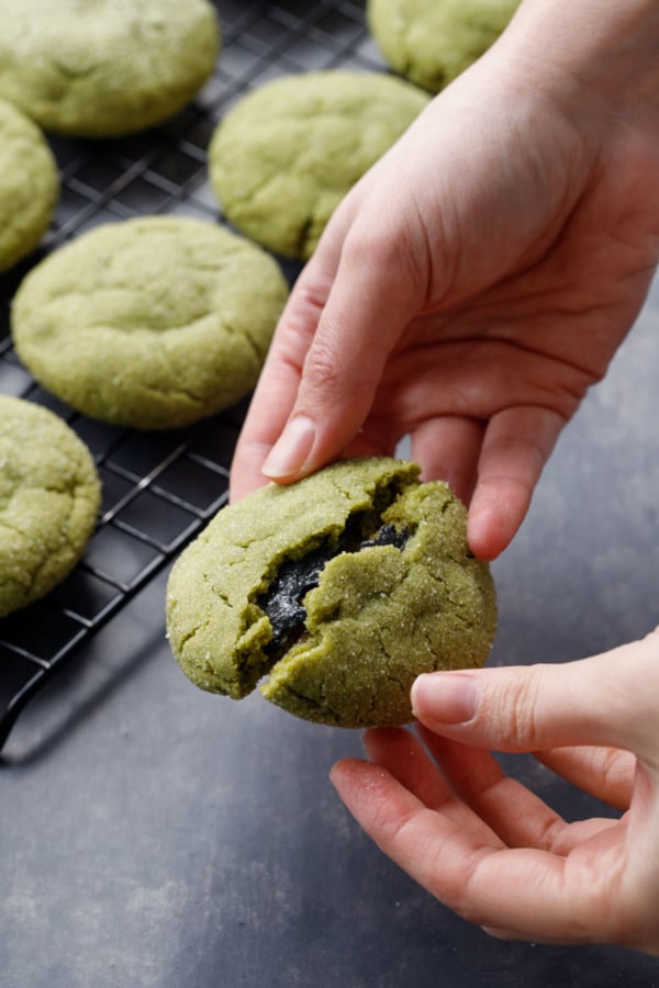 Green matcha sugar cookie broken in half to reveal the black sesame filling