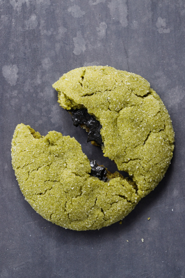 Green matcha sugar cookie broken in half to reveal the black sesame filling