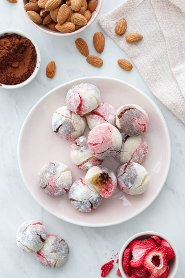 Overhead of plate of Neapolitan Amaretti Cookies with bowls of cocoa powder, almonds and freeze-dried strawberries