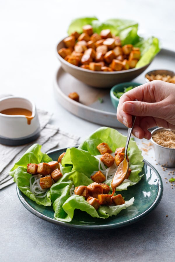 Spooning spicy peanut sauce onto Baked Tofu Lettuce Wraps