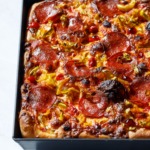 Detroit-style pan pizza styled in harsh light topped with pepperoni and pickled peppers.