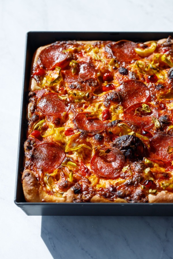 Detroit-style pan pizza styled in harsh light topped with pepperoni and pickled peppers.