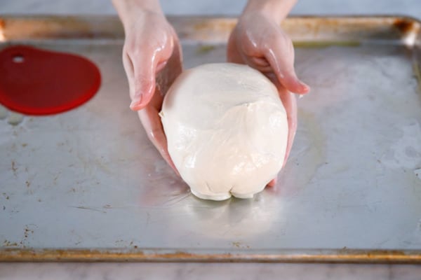Shaping the pizza dough on an oiled sheet pan.