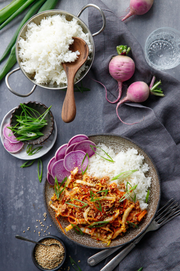 Overhead shot of bowl of Spicy Korean Egg Roll Bowls with a dish of white rice and purple radishes.