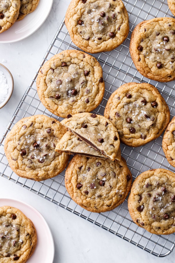 Overhead of Ganache-Stuffed Chocolate Chip Cookies on a wire rack with a small bowl of flake sea salt