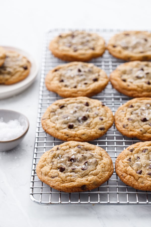 Ganache-Stuffed Chocolate Chip Cookies on a wire cooking rack with a small bowl of flake sea salt