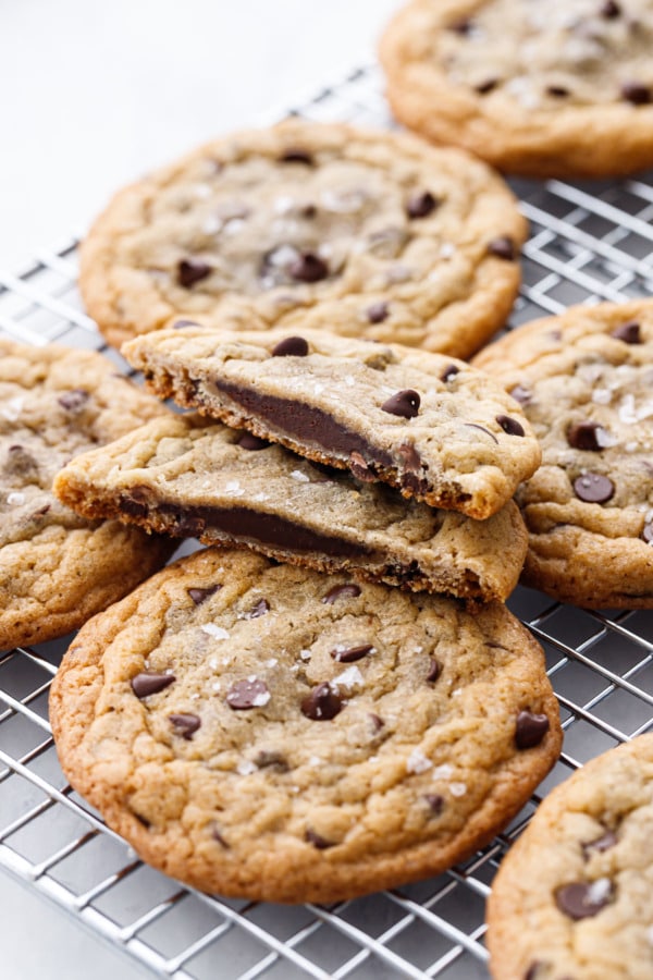 Ganache-Stuffed Chocolate Chip Cookies on a wire rack, one cookie cut in half to show the ganache filling