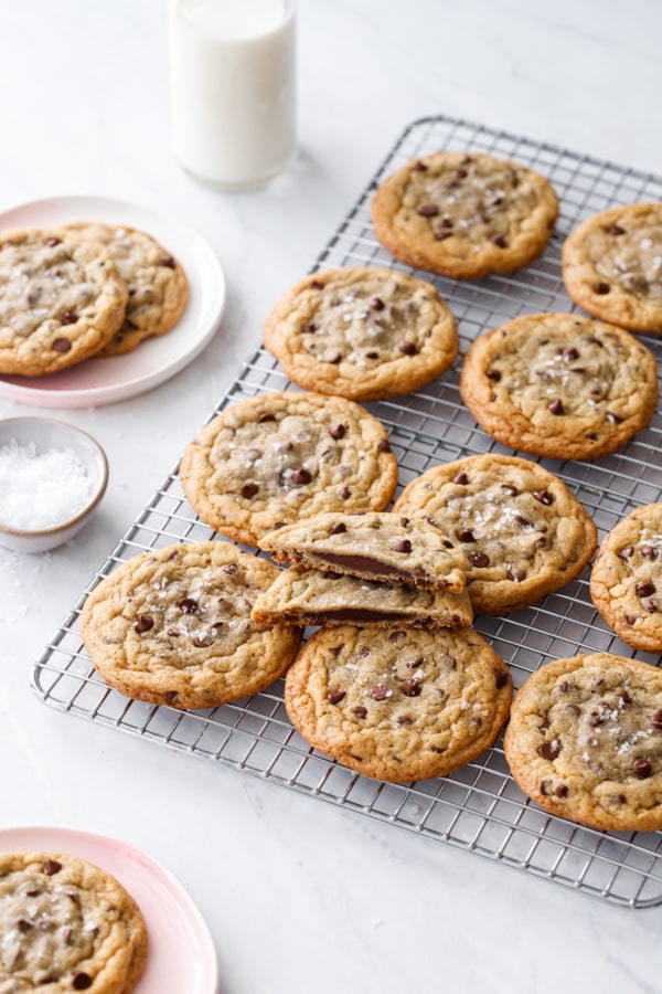 Ganache-Stuffed Chocolate Chip Cookies on a wire rack with a bowl of flake salt and milk bottle.