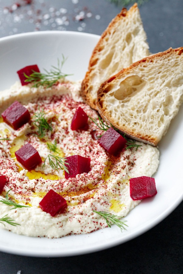 Closeup of white bowl with Whipped Almond Dip, topped with Pickled Beets, fresh dill and two slices of Sourdough