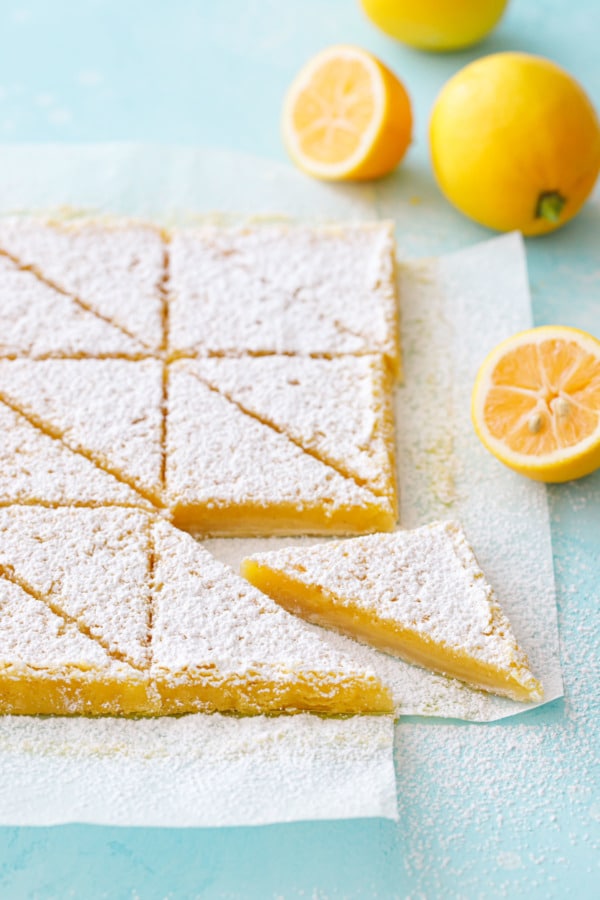 Sliced Meyer Lemon Bars on a light turquoise background with whole and halved Meyer lemons.