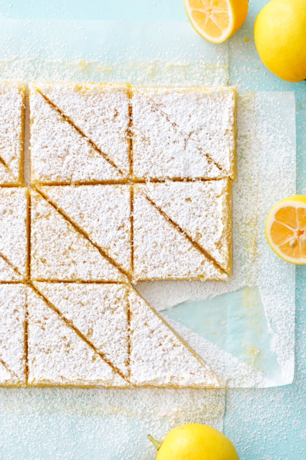 Meyer Lemon Bars on a turquoise background, cut into triangles and dusted with powdered sugar