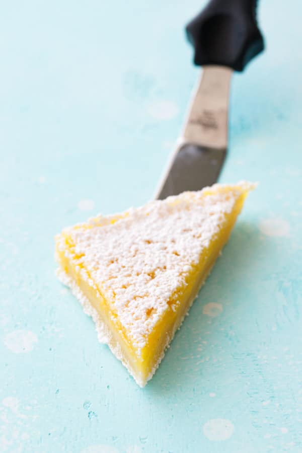 Triangle sliced Meyer Lemon Bar on a spatula, on a turquoise background.