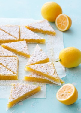 Stacks of sliced Meyer Lemon Bars on a turquoise background, with whole and half Meyer lemons