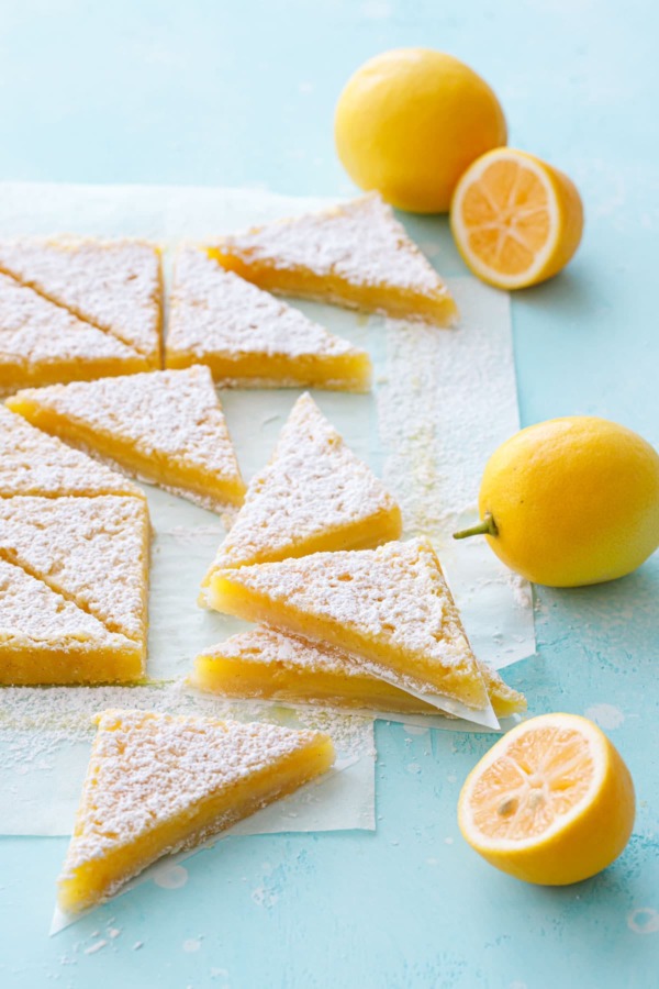 Stacks of sliced Meyer Lemon Bars on a turquoise background, with whole and half Meyer lemons