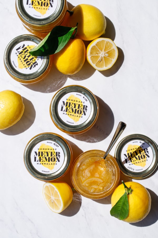 Overhead of jars of Old-Fashioned Meyer Lemon Marmalade and whole/halved lemons with leaves.