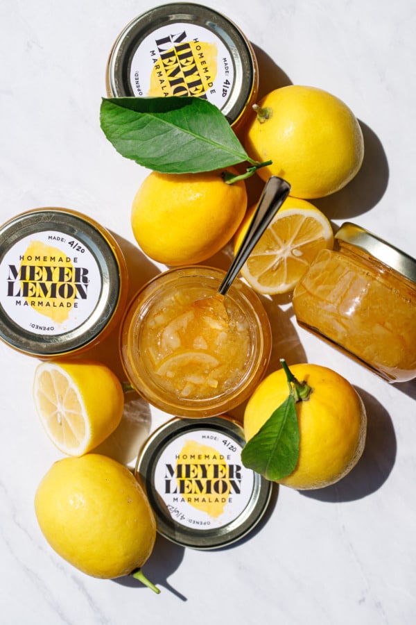 Overhead of jars of Old-Fashioned Meyer Lemon Marmalade and whole/halved lemons with leaves.