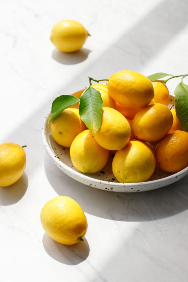 Bright yellow Meyer lemons in a ceramic bowl on marble background