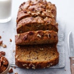 Sliced Bananas Foster Banana Bread with knife and pecans and a glass of milk