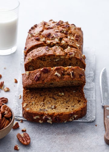 Sliced Bananas Foster Banana Bread with knife and pecans and a glass of milk